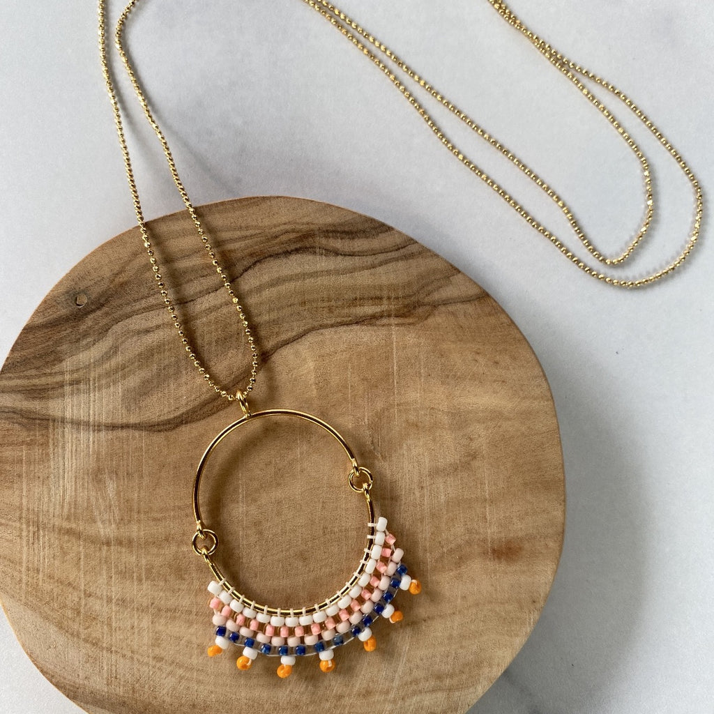Handmade in Guatemala for New York jewelry line Bluma Project.  This necklace features handmade beading on a gold-plated arc pendant hanging from a gold plated chain.  White, pink, navy, and orange beads are a summery, easy to wear palate.